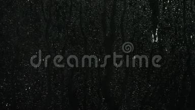 雨滴溅在黑色背景上的玻璃上。 库存录像。 <strong>雨水</strong>背景，滴在玻璃上